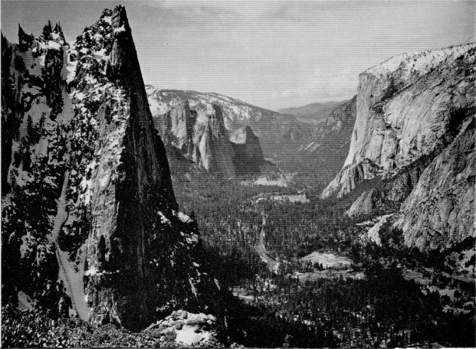 A view down Yosemite Valley from the trail above Union Point showing the broad U-shape of the chasm. Sentinel Rock. Cathedral Rocks, and El Capitan. By Ansel Adams